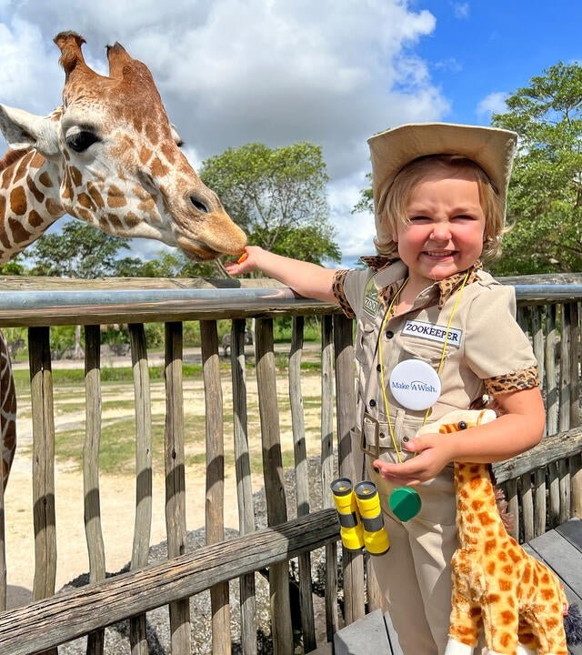 Wish kid Amelia dressed like a zookeeper feeding a giraffe