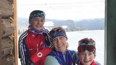 Dr Carlson sits between her two children in a cabin, with snow and trees in the background