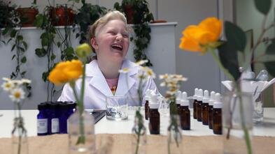 Monika smiling in the lab surrounded with fragrance bottles and yellow flowers