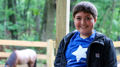Maddie posed, smiling and wearing her Make-A-Wish star t-shirt, with horse in background