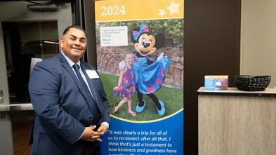 Volunteer John Villanueva at Wish Insiders Monterey standing next to a popup sign for Make-A-Wish Greater Bay Area's first wish