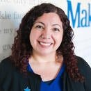 Jennifer Varela, Wish Referral Specialist, smiling in front of the Wish Wall