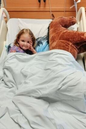 Wish kid Mary Alice sitting in a hospital bed with her stuffed horse toy